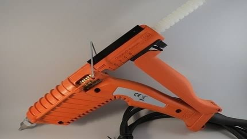 Close-up of an industrial orange hot glue gun with power cable and glue stick inserted