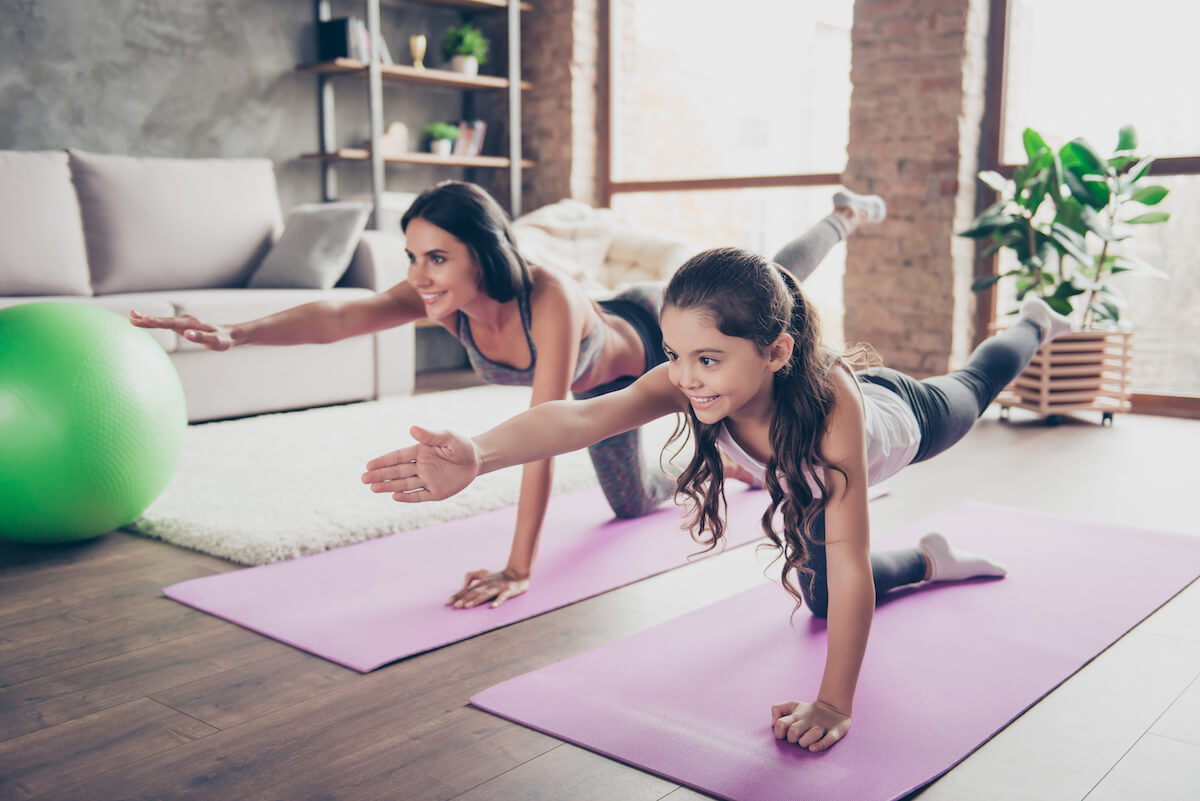 A mother and daughter doing power yoga and breathing deeply as human services recommends with right foot up for better fitness