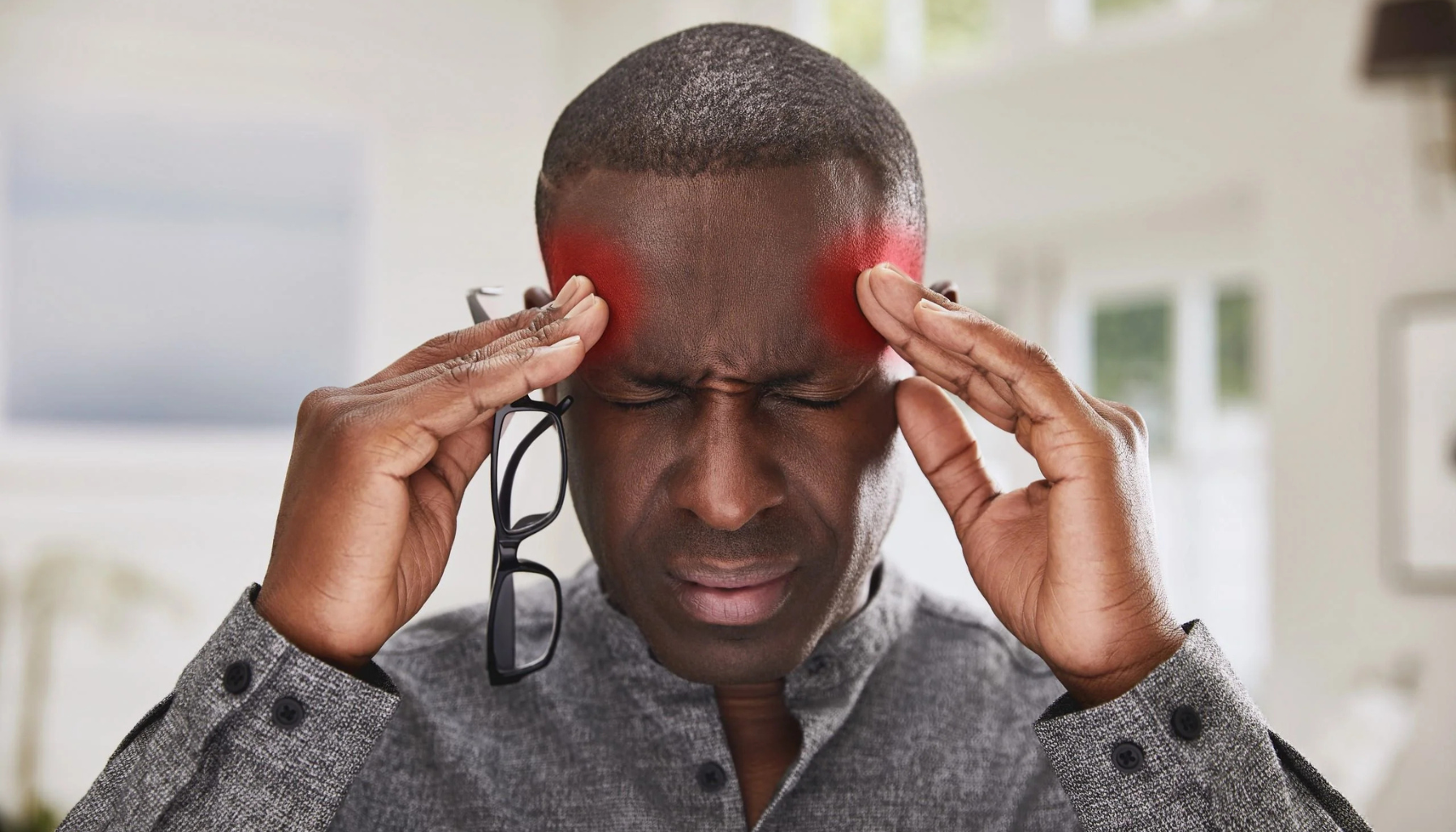 Spenningshodepine: mann holder hodet; røde områder ved tinninger illustrerer trykkende smerte.