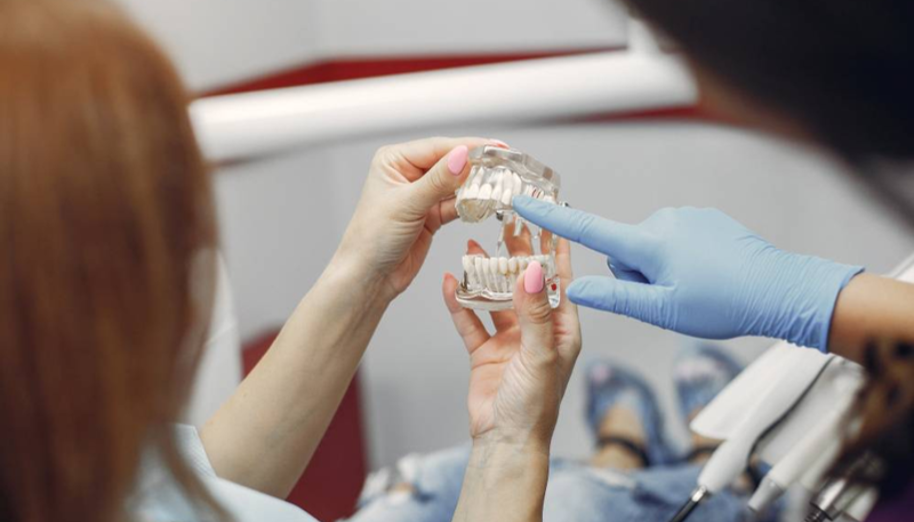 "Tannlege med hansker forklarer pasient ved å peke på en tannmodell som viser tenner og kjeve."