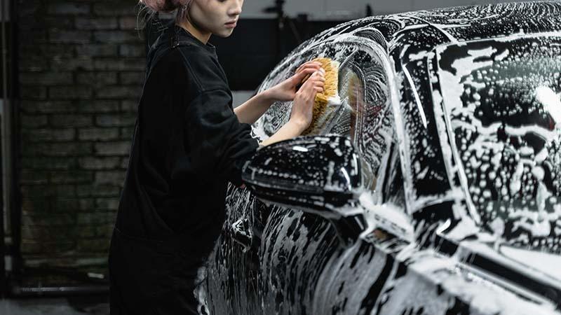 A girl washing a black car with warm water and soap