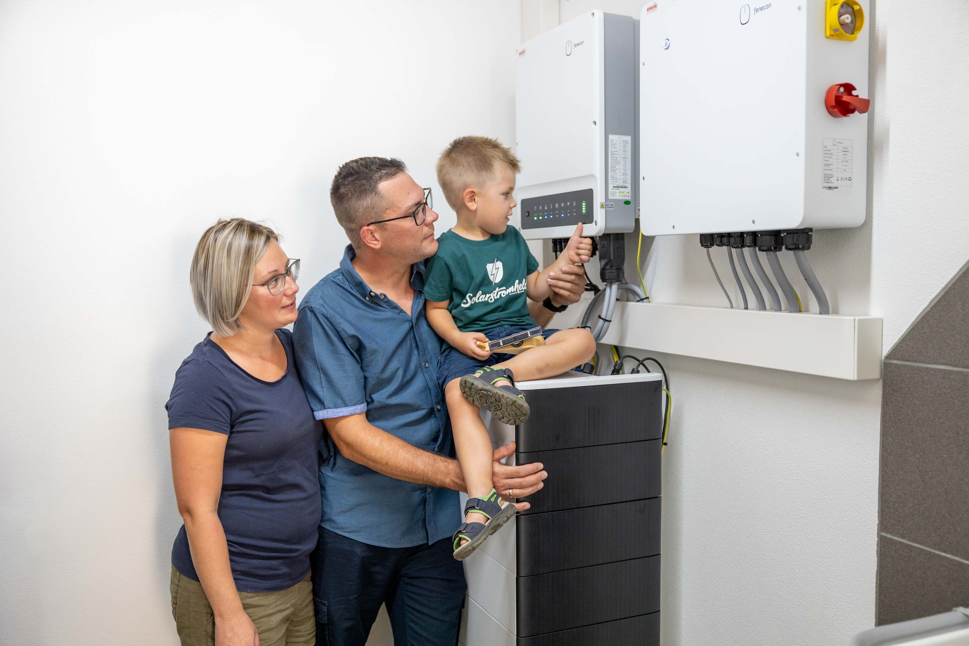 Eine Familie vor einem Stromspeicher und Wechselrichter. 