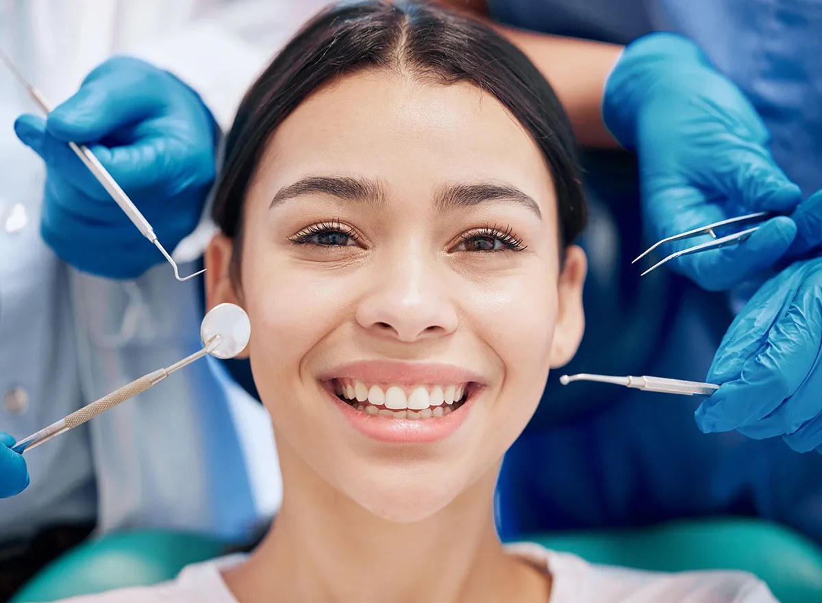 Smiling dental patient during examination with multiple dental instruments positioned around teeth, showcasing modern dental examination procedures.