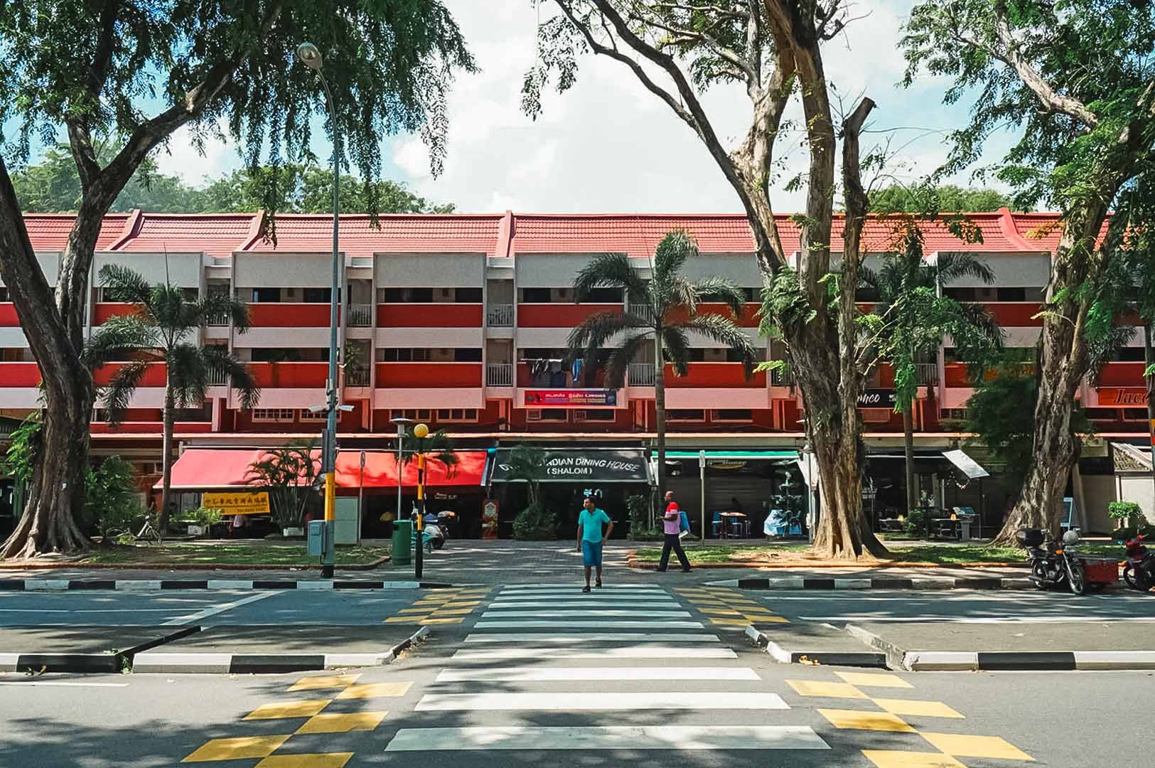 Pedestrian crossing leading to a row of Changi Village shops beneath red‑roofed housing blocks.