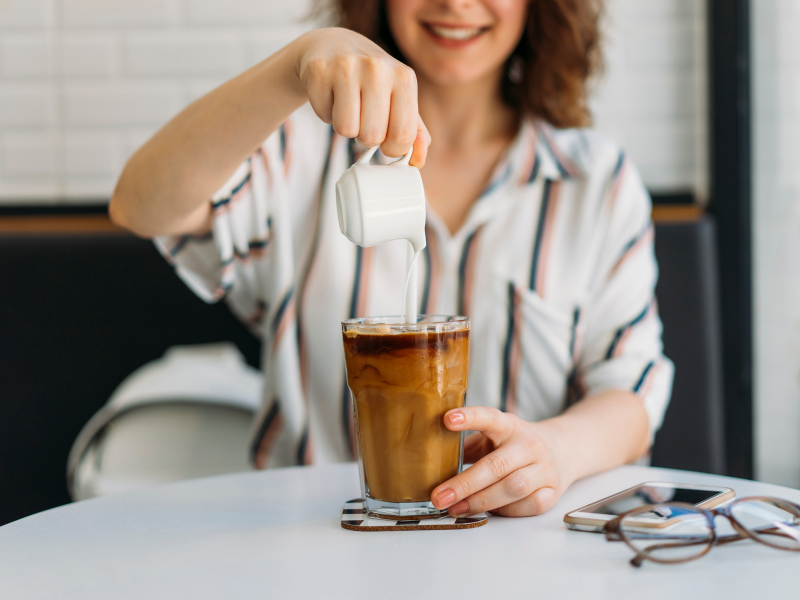 Mulher despeja leite sobre cold brewed coffee. Foto: hsyncoban de Getty Images - Canva.