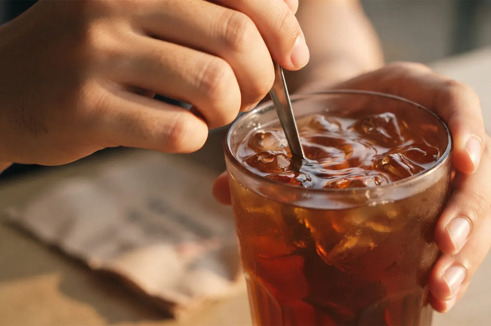 Person stirring a glass of iced tea with a metal spoon.
