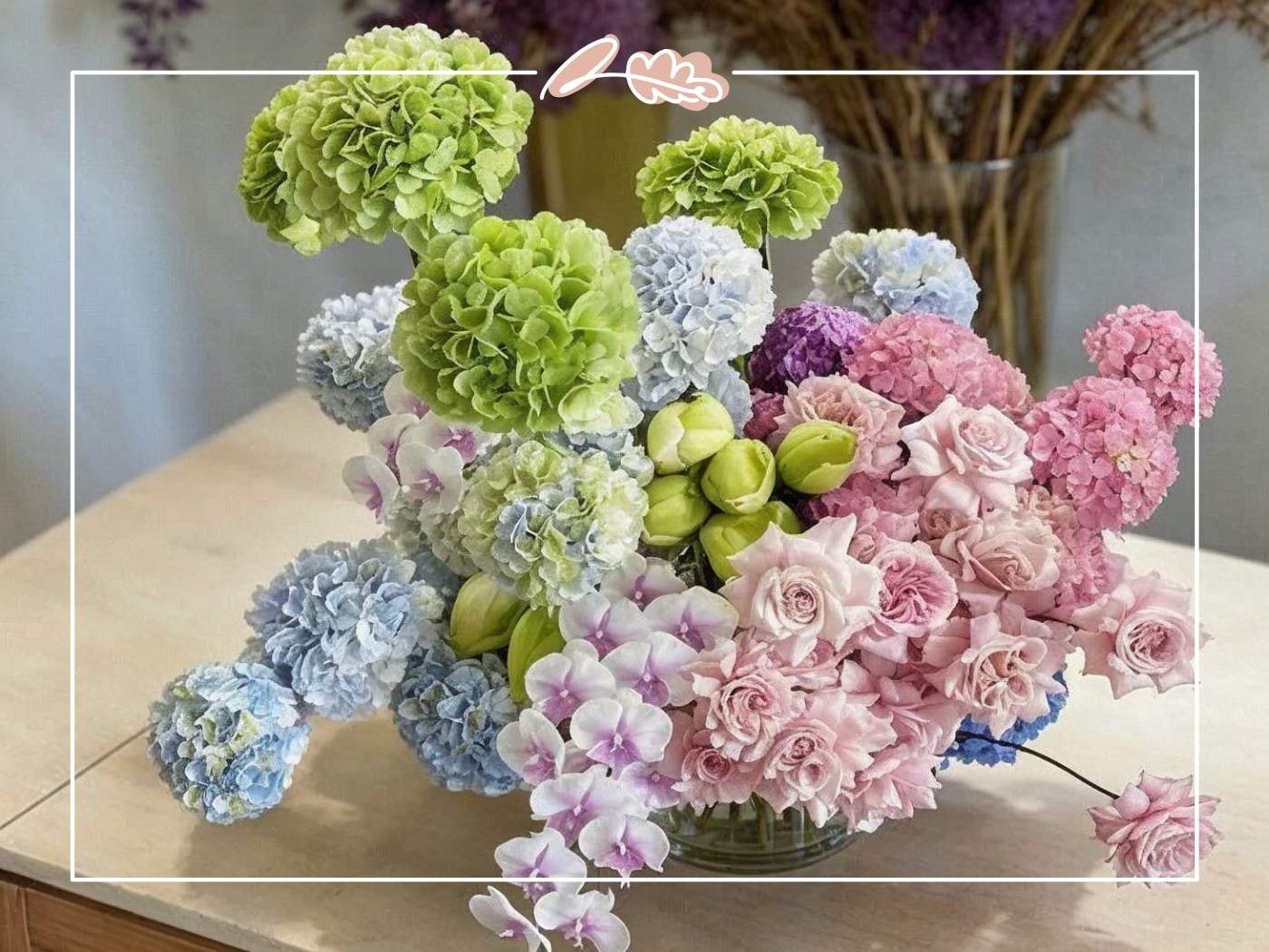 Elegant hydrangea flower arrangement with blue, green, and pink hydrangeas paired with blush roses and orchids in a glass vase