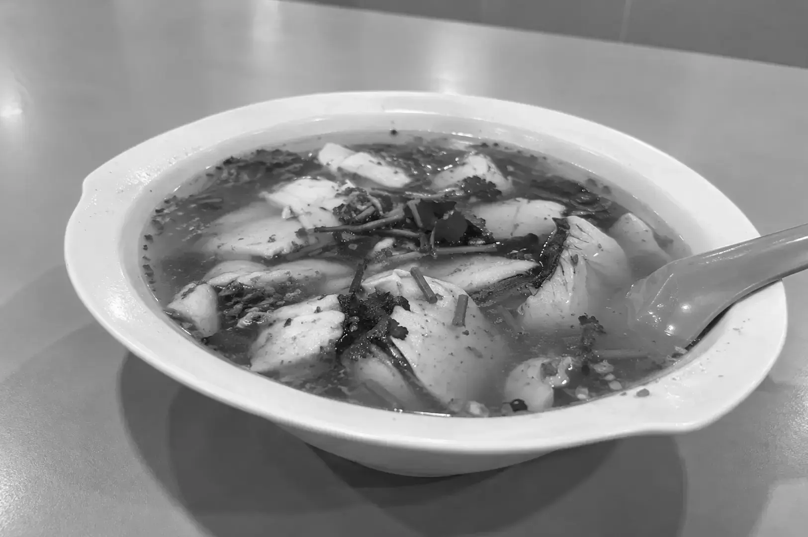 A bowl of Sliced Fish Bee Hoon with tender fish slices, noodles, prawns, and vegetables in a clear savory broth.