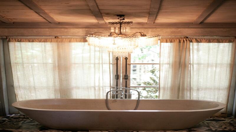 Symmetrical View of a Bathtub on a Carpet and Crystal Chandelier Hanging from a Wooden Ceiling