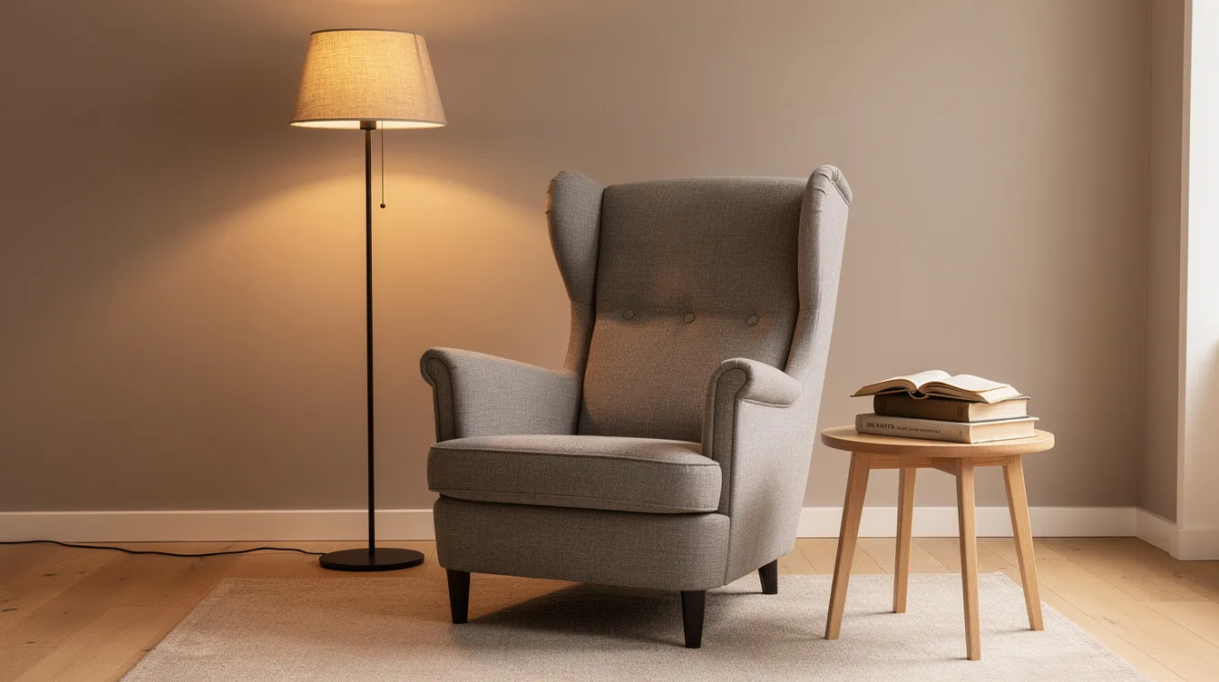 En mysig läshörna med en grå hög fåtölj, som har hög rygg och armstöd, står i rummet. Bredvid fåtöljen finns en golvlampa och ett sidobord fyllt med böcker, vilket skapar en perfekt plats för avkoppling och läsning.