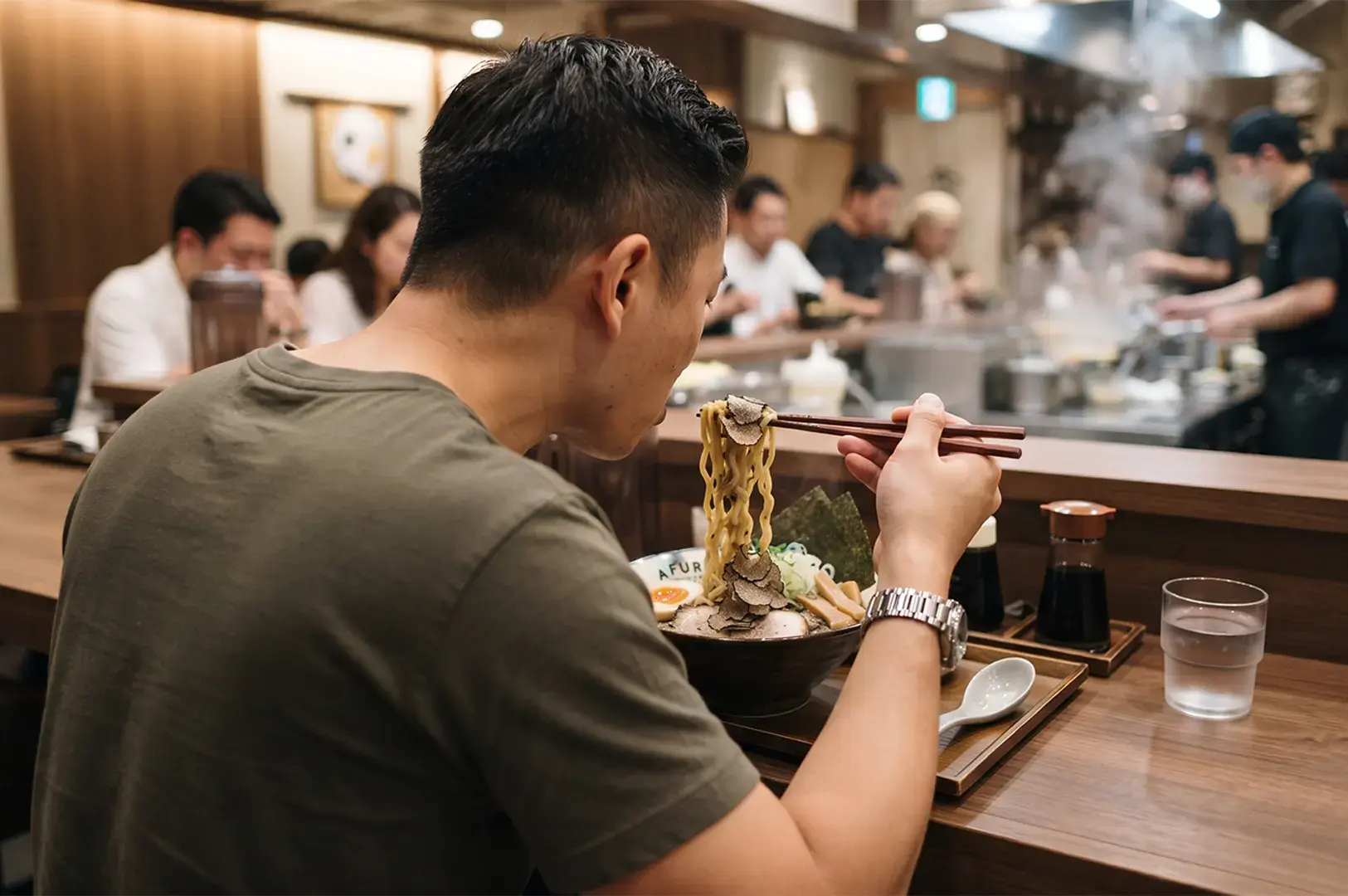 Man eating a bowl of truffle ramen with chopsticks at a restaurant counter.