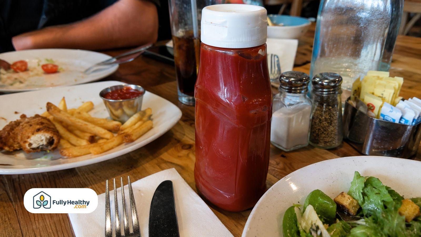 Ketchup bottle sitting on restaurant table near fries and meal.