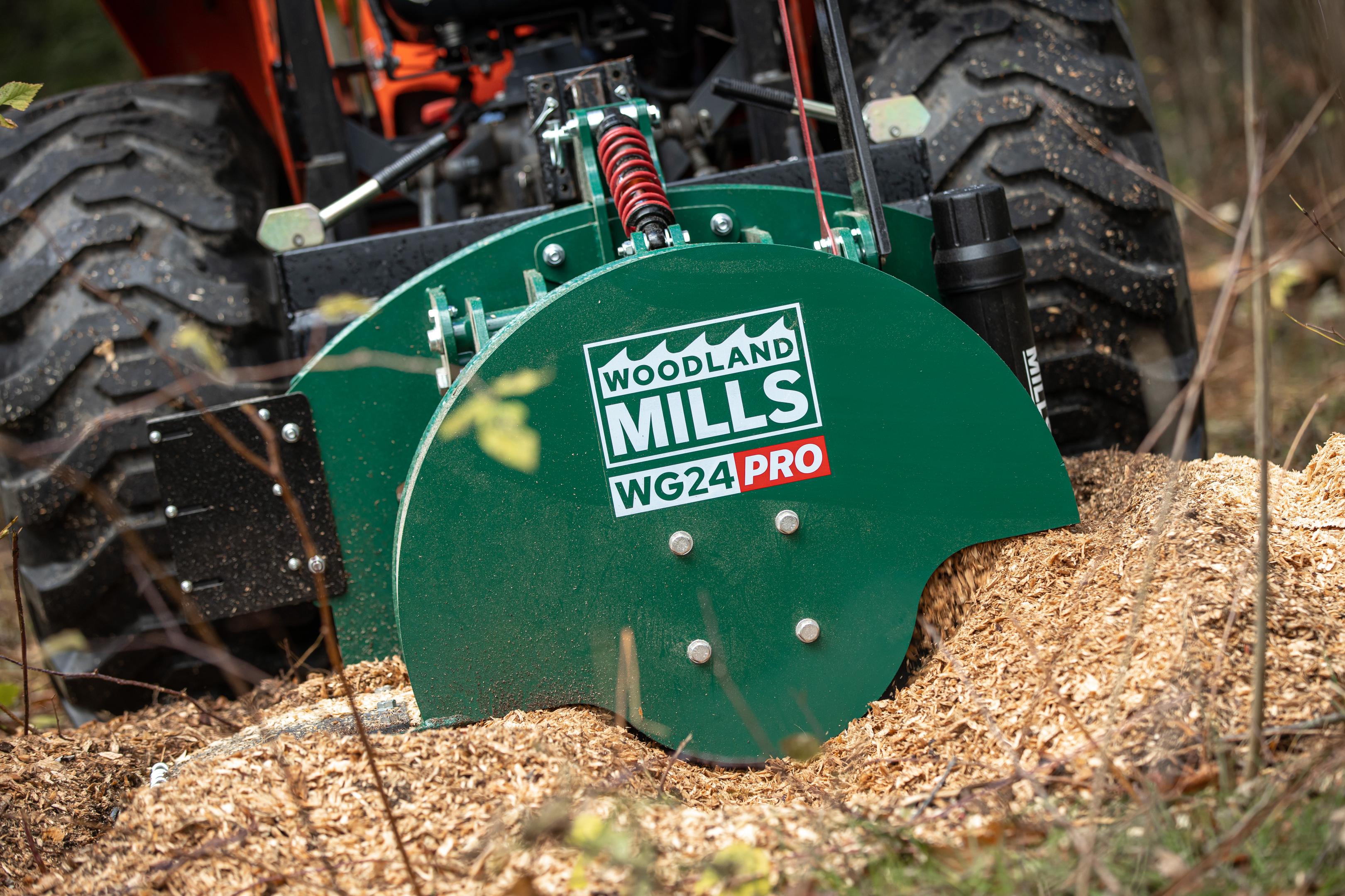 A Woodland Mills WG24 PRO stump grinder embedded in the dirt, surrounded by wood chips.