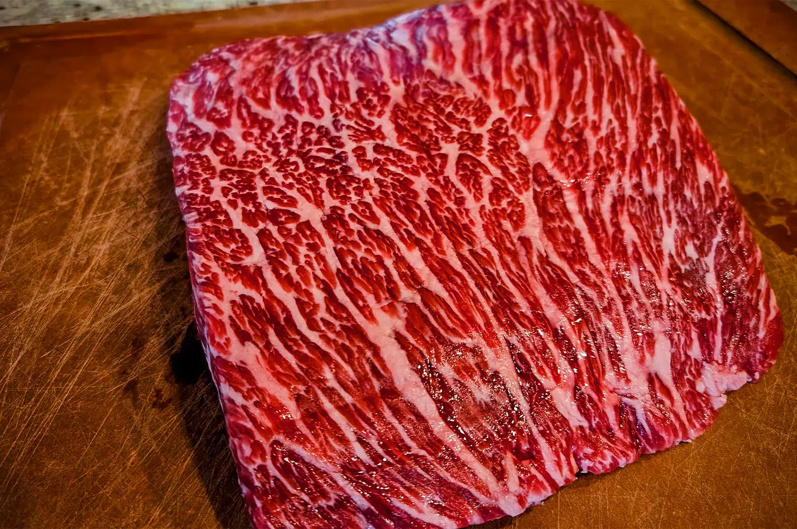 Close-up of a raw steak with intense marbling, displaying rich red meat interwoven with white fat, on a wooden cutting board.