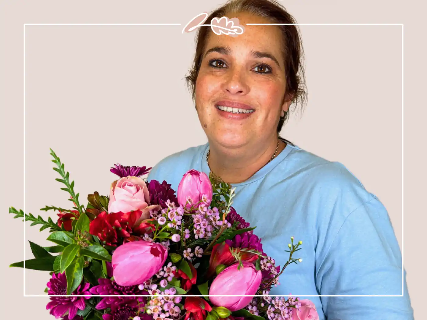 A woman in a light blue top holding a bouquet of pink and red flowers, smiling warmly.