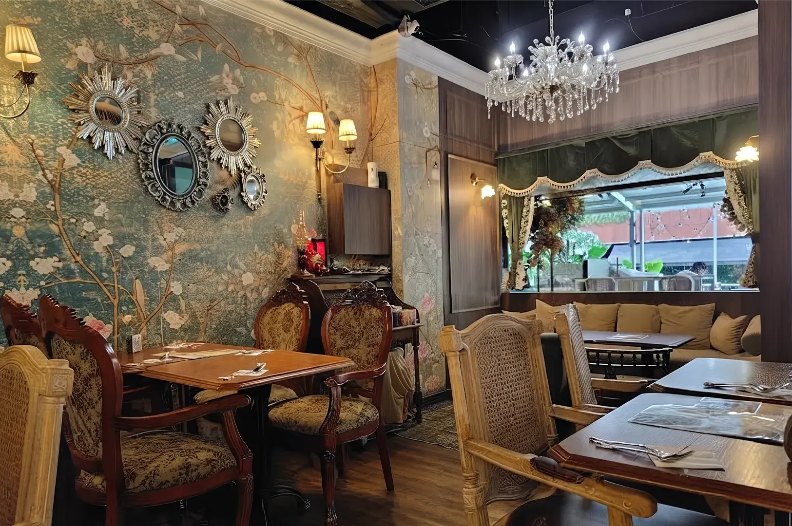 Vintage restaurant dining room with floral wallpaper, crystal chandelier, and damask armchairs.