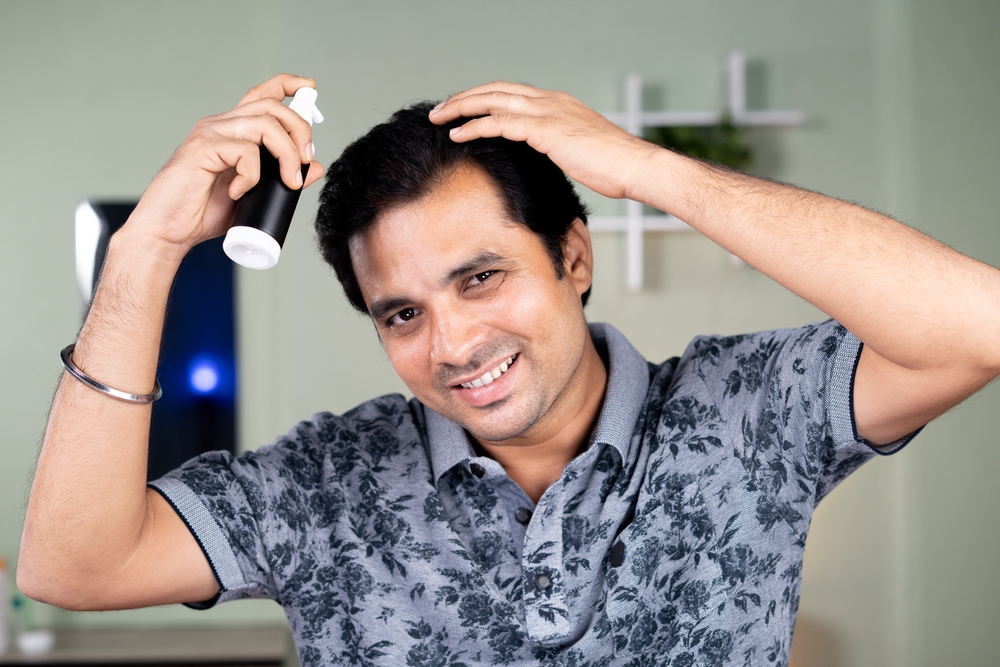 Man applying minoxidil spray to hair