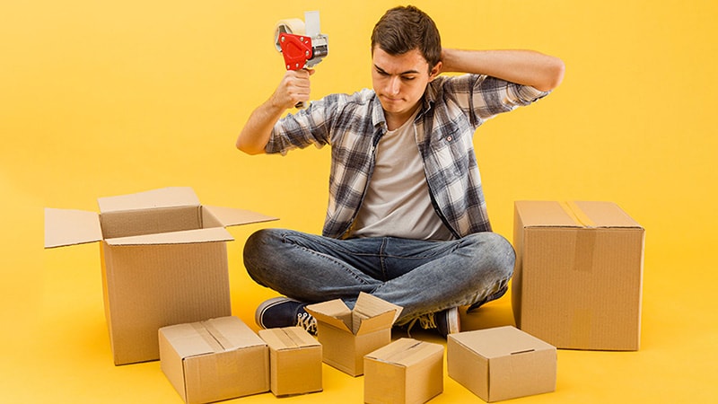A man is trying to package items in cardboard boxes