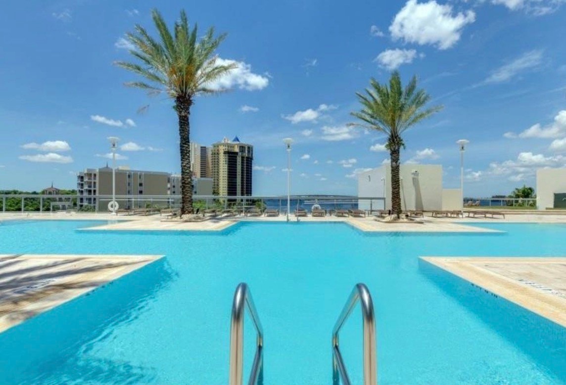 The image showcases the spacious interior of a luxury waterfront residence in Fort Myers, featuring elegant granite countertops and floor-to-ceiling windows that provide unobstructed panoramic views of the Caloosahatchee River and the vibrant city skyline. This exceptional condo offers a perfect setting to enjoy relaxing evenings while admiring the famous Florida sunsets from your private balcony.
