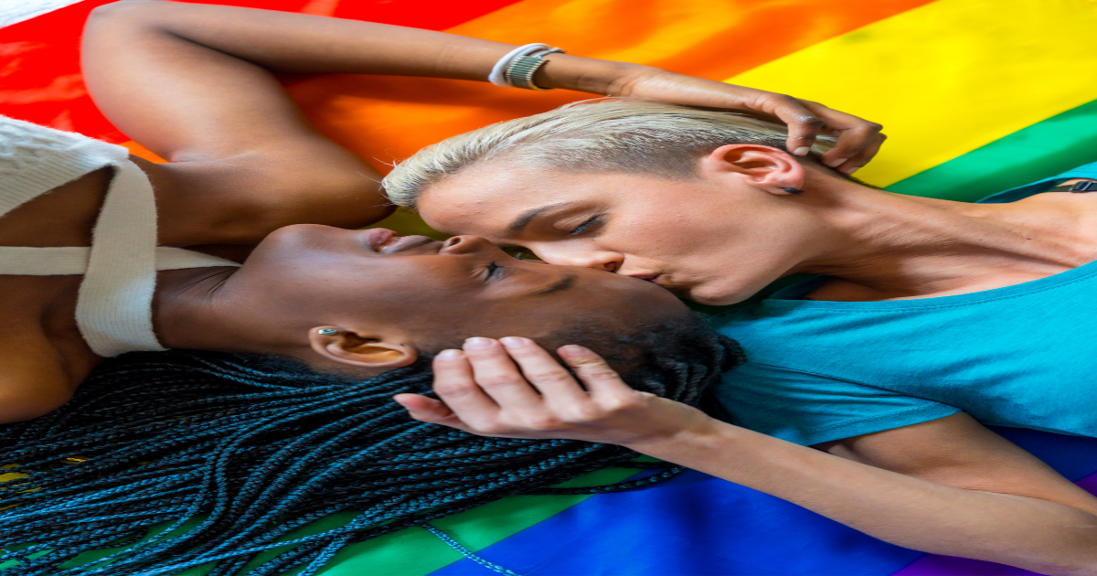 A photograph of a lesbian couple standing close together, with one partner holding the other's face and kissing her on the lips. The background features an LGBTQ pride flag, symbolizing the couple's pride and joy in their relationship. The image conveys the idea of a couple who have successfully undergone Gottman Method Couples Therapy in New York City and have emerged with a stronger emotional connection and greater intimacy. The couple appears happy and in love, indicating that therapy has helped them overcome previous conflicts or difficulties in their relationship.