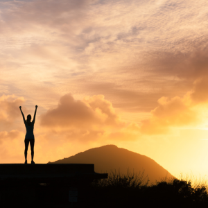 a person in the distance with their hands up at sunset