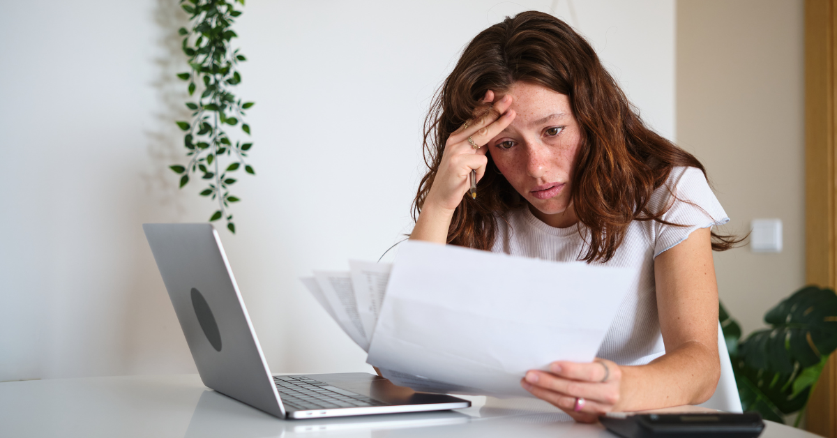 A young creator at her desk looking confused with bills, laptop, and calculator, wondering is accounts receivable an asset or liability for OnlyFans taxes.