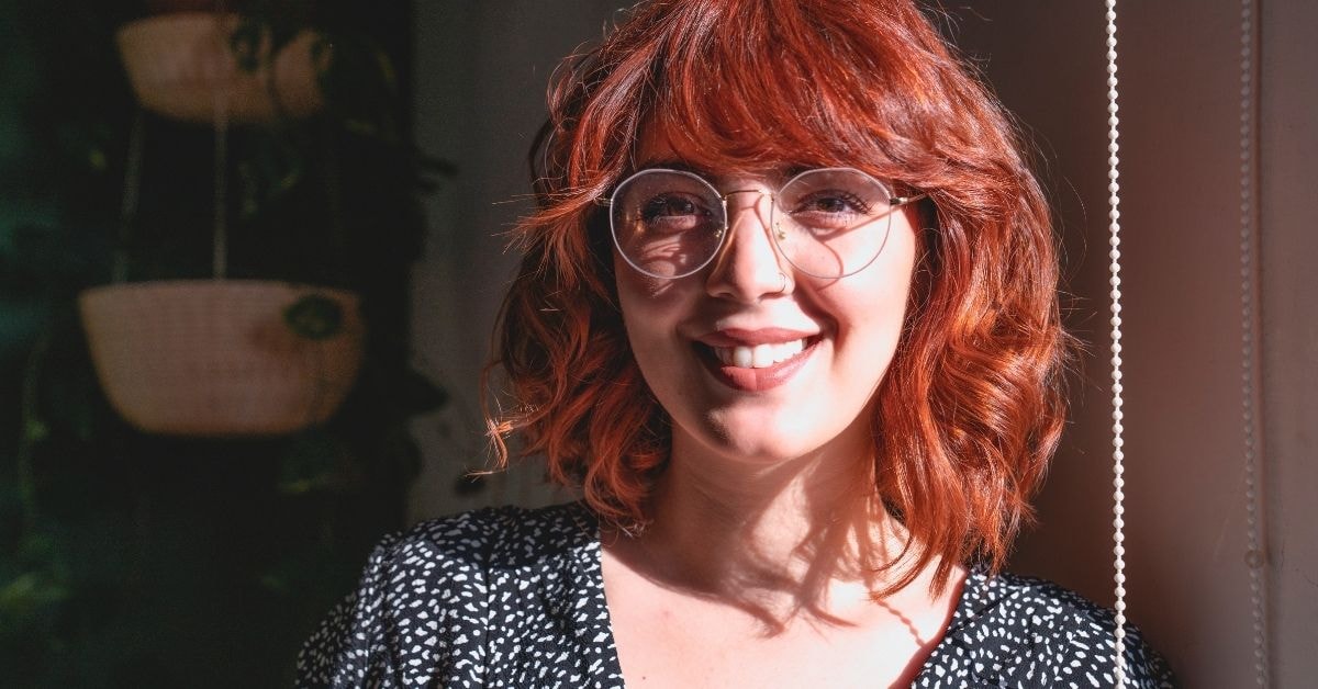 Smiling woman with curly red hair and glasses, representing a confident OnlyFans creator.