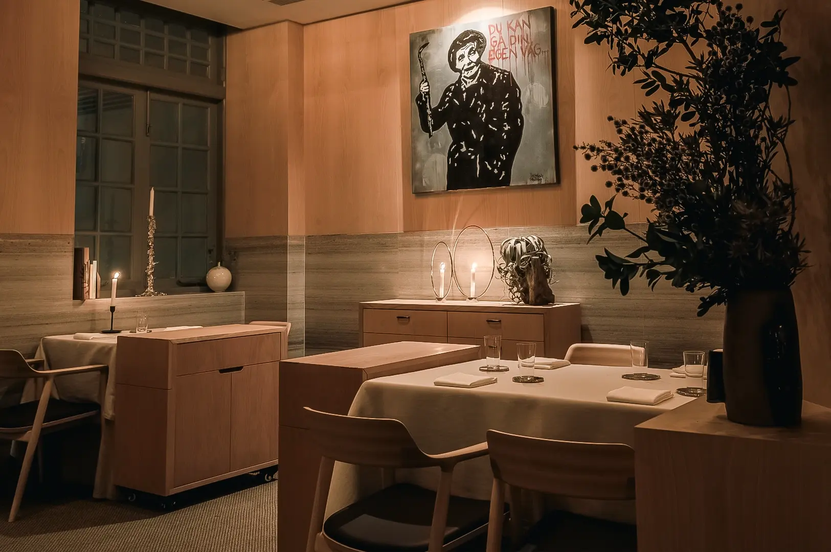Eye‑level medium wide shot of an intimate chef’s table dining room, showcasing wood‑paneled walls, curated artwork, soft ambient lighting, and a neatly set communal table.