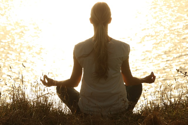 Woman sitting in lotus position, meditating in front of peaceful lake. 