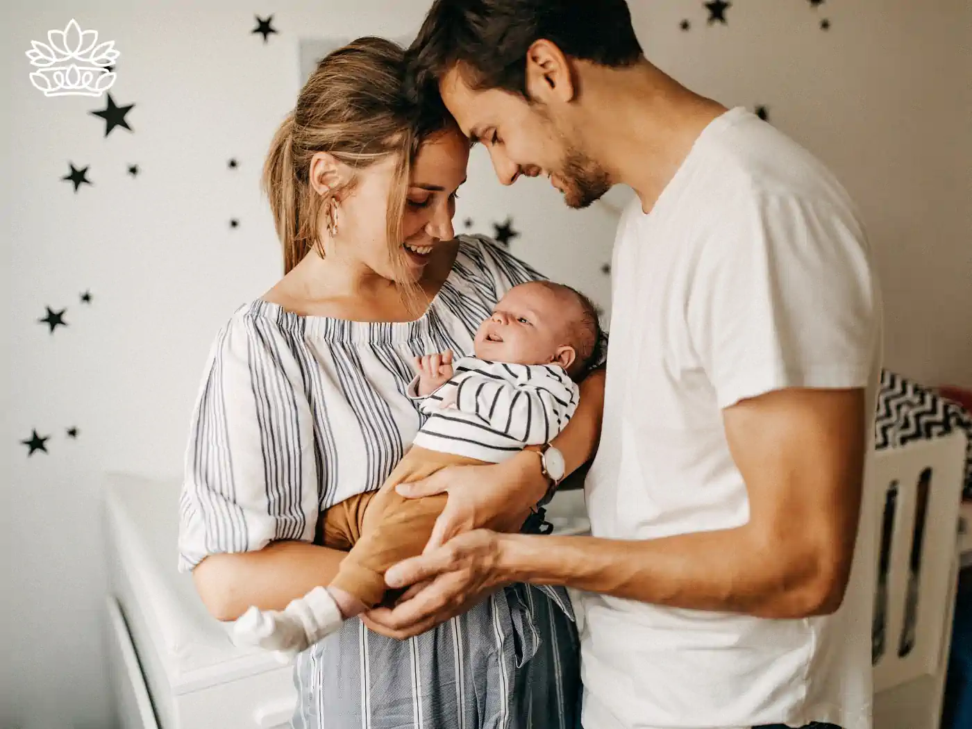 Parents holding their newborn baby and smiling in a star-decorated room. Fabulous Flowers and Gifts. New Baby Flowers British English.
