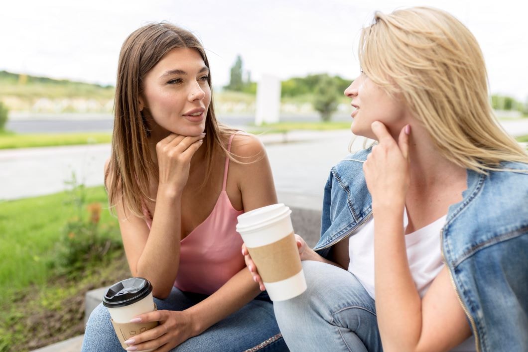 Zwei Frauen mit Trinkbecher in der Hand unterhalten sich im Sitzen