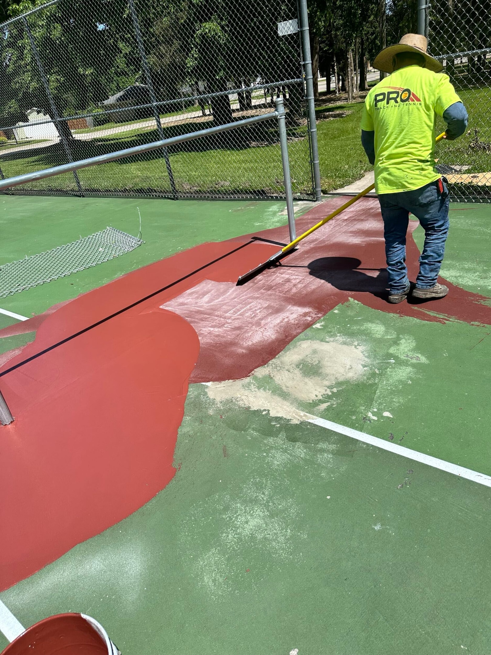Pro Track and Tennis crew working on a court resurfacing project, painting the surface for restoration.
