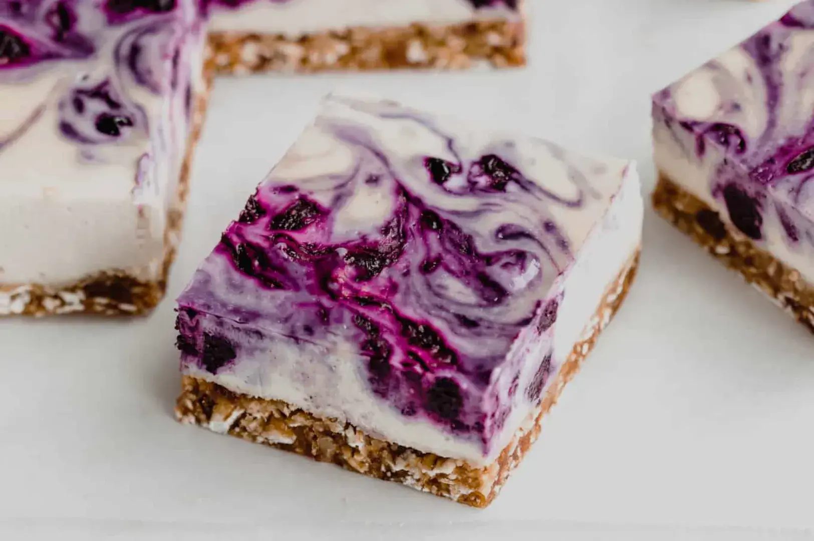 A square piece of swirl cheesecake with a berry topping on a graham cracker crust.