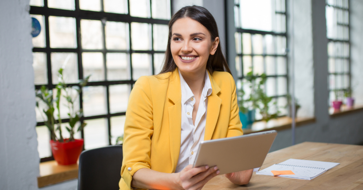 A smiling woman in a bright office holding a tablet; wondering how much does the IRS spends on tax audits.