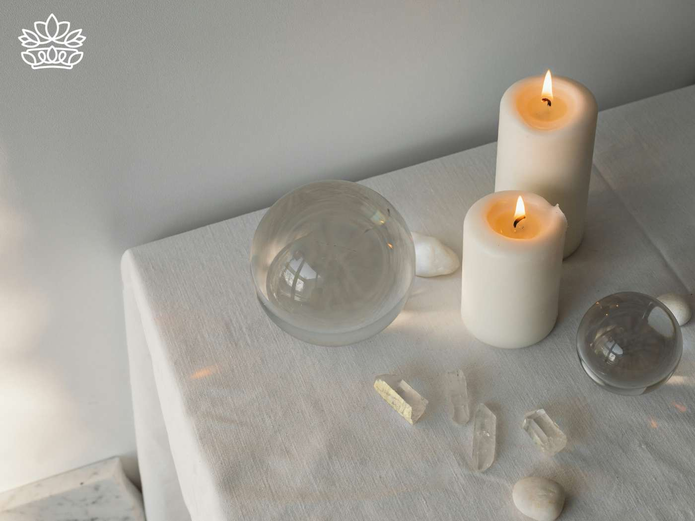 A tranquil setting featuring lit pillar candles alongside spherical glass accents and scattered quartz pieces, casting a warm glow over the tableau, part of the Candles Collection - Fabulous Flowers and Gifts.