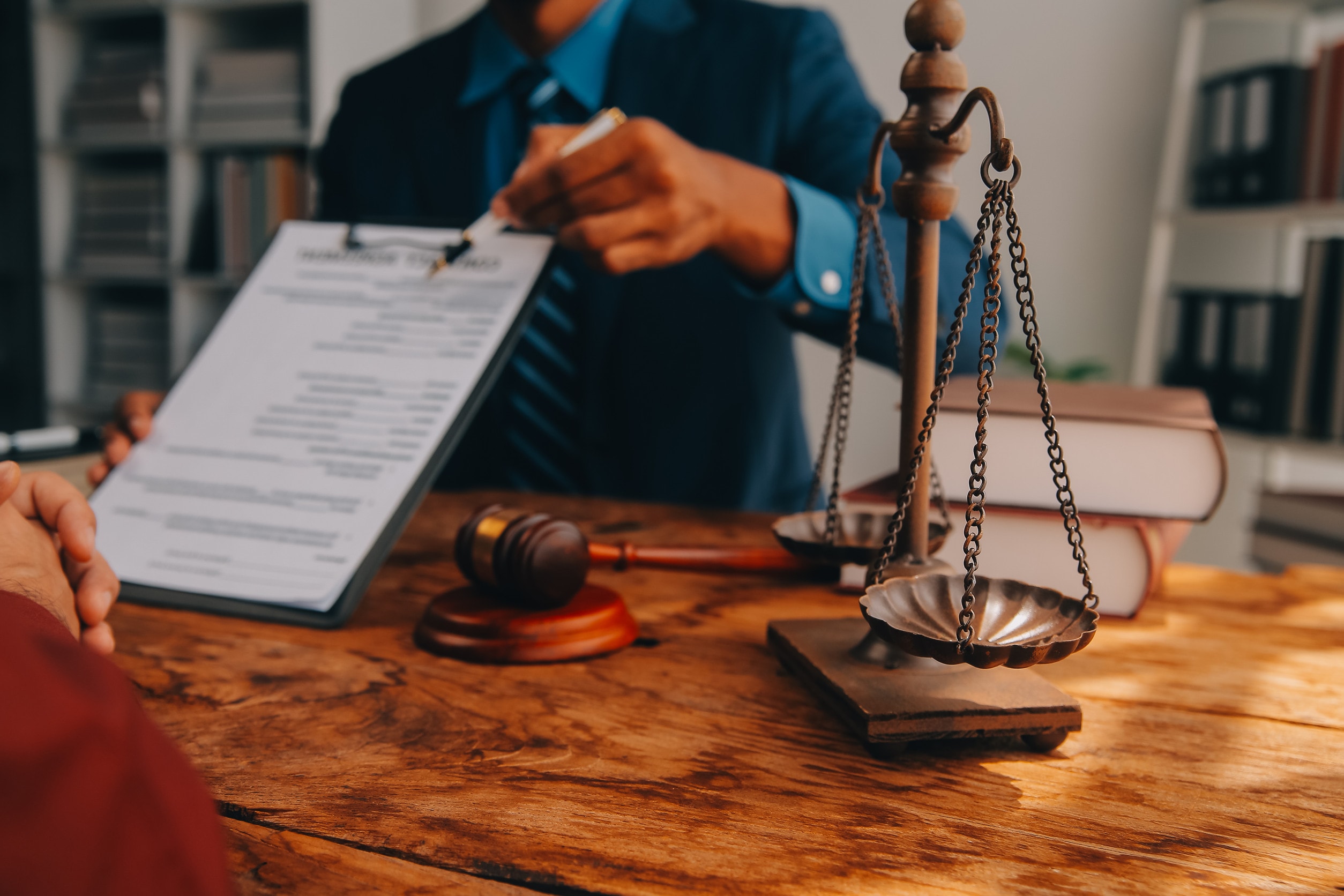 A lawyer holds a contract out to a client while sitting behind a desk