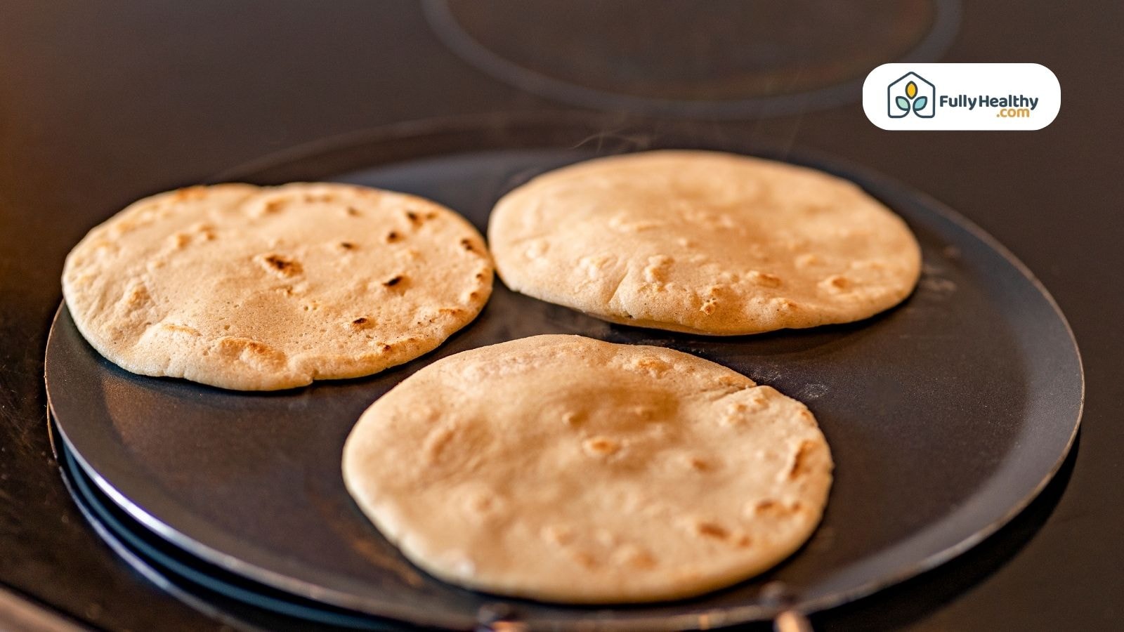 Three tortillas cooking on a flat pan or griddle