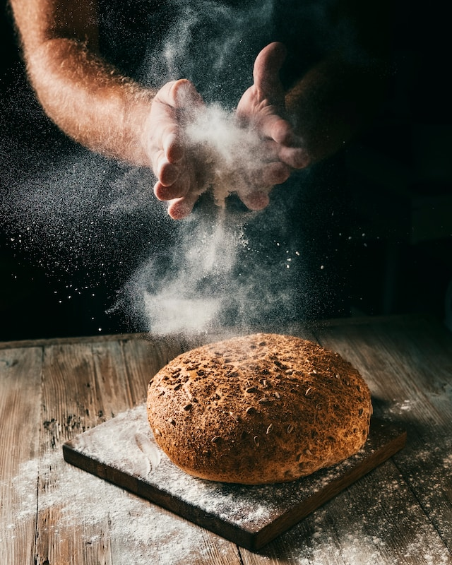 hands making flour cloud under baked bread