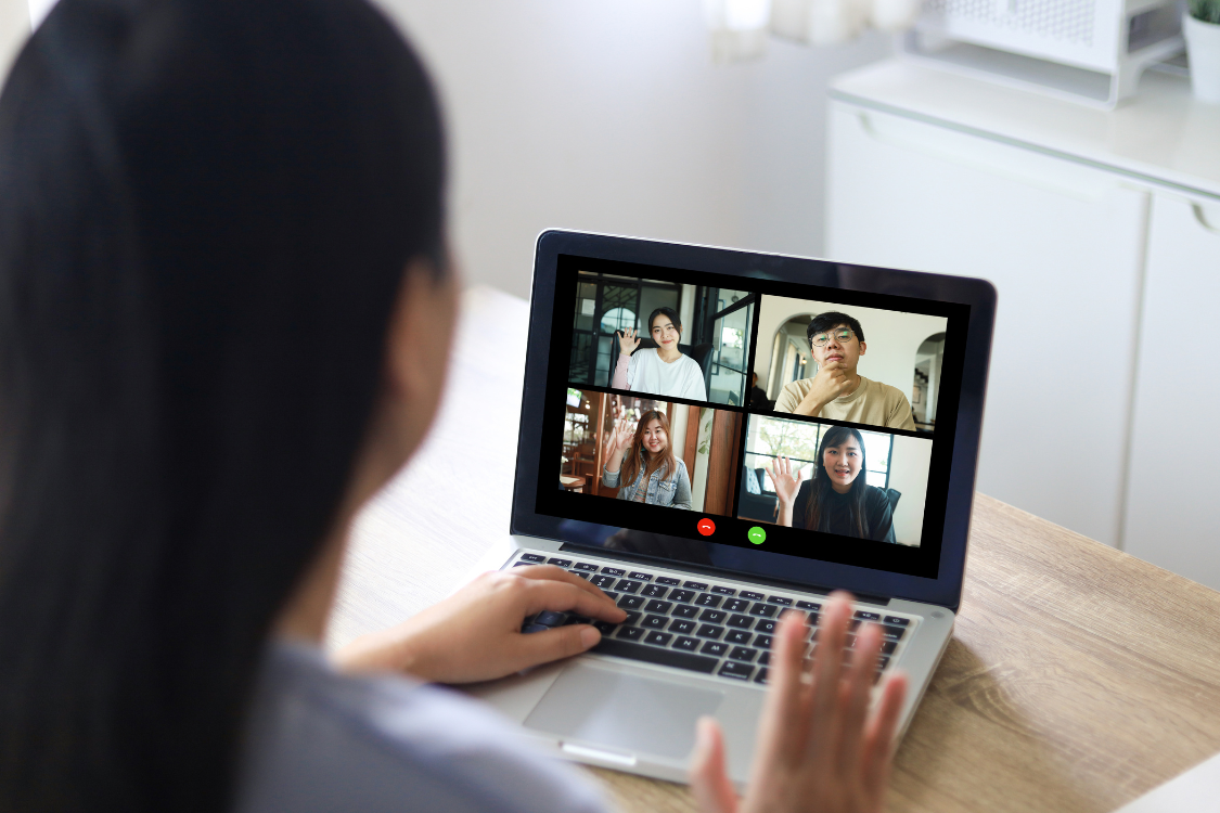 Team video conference with four Filipino professionals waving at their remote teammate