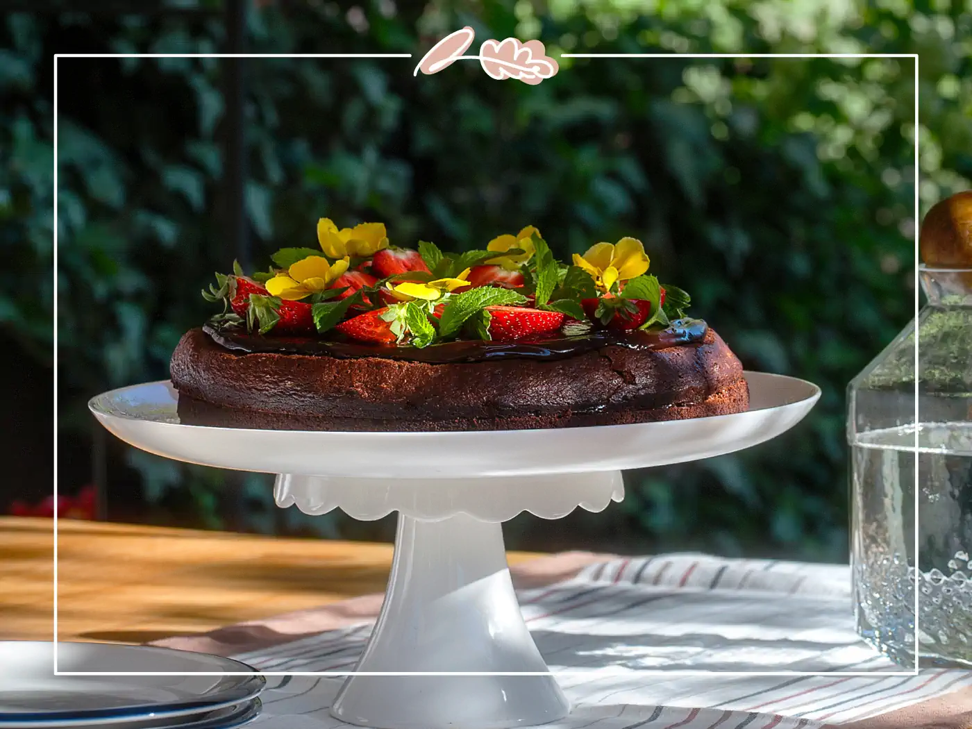 Chocolate cake topped with fresh strawberries and edible flowers on a cake stand. Fabulous Flowers and Gifts.