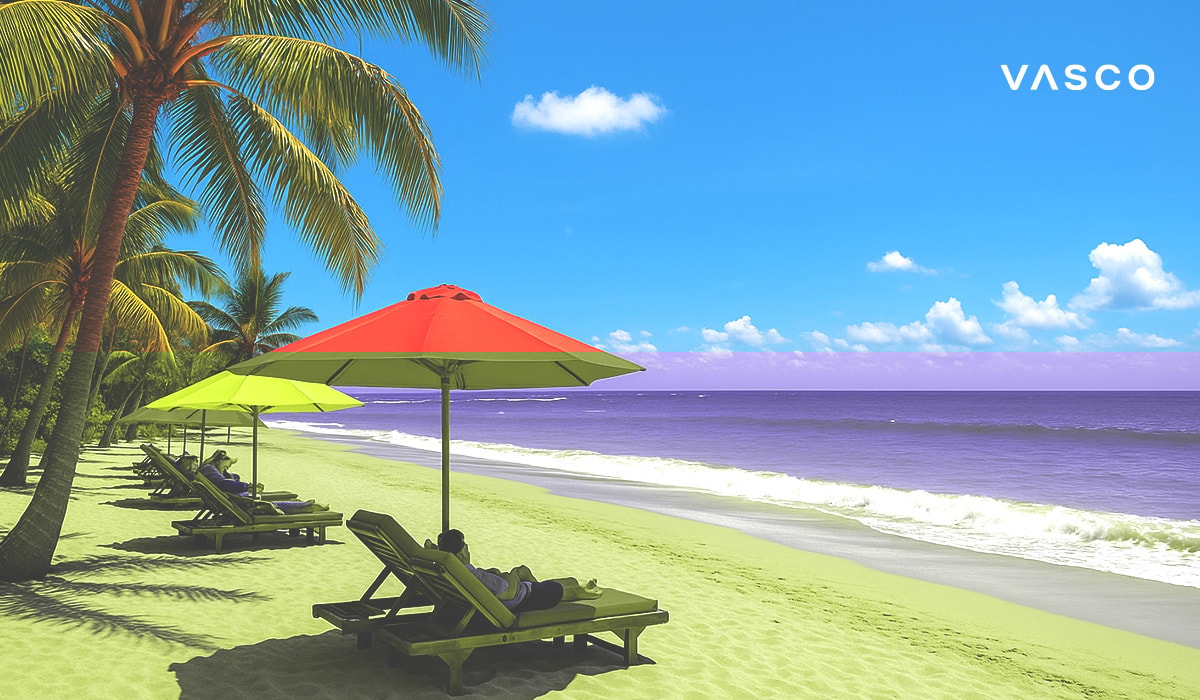 Tourists relaxing on sun loungers under red and yellow umbrellas on a beautiful sandy beach with turquoise water.