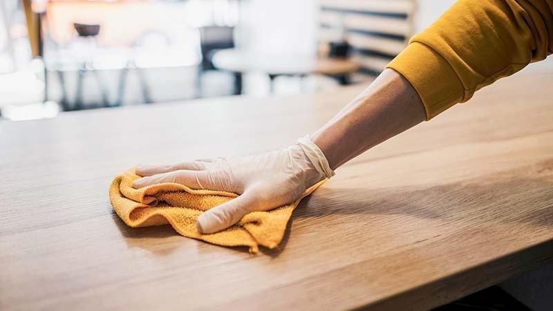 A man cleaning a restraunt table with a yellow microfiber towel