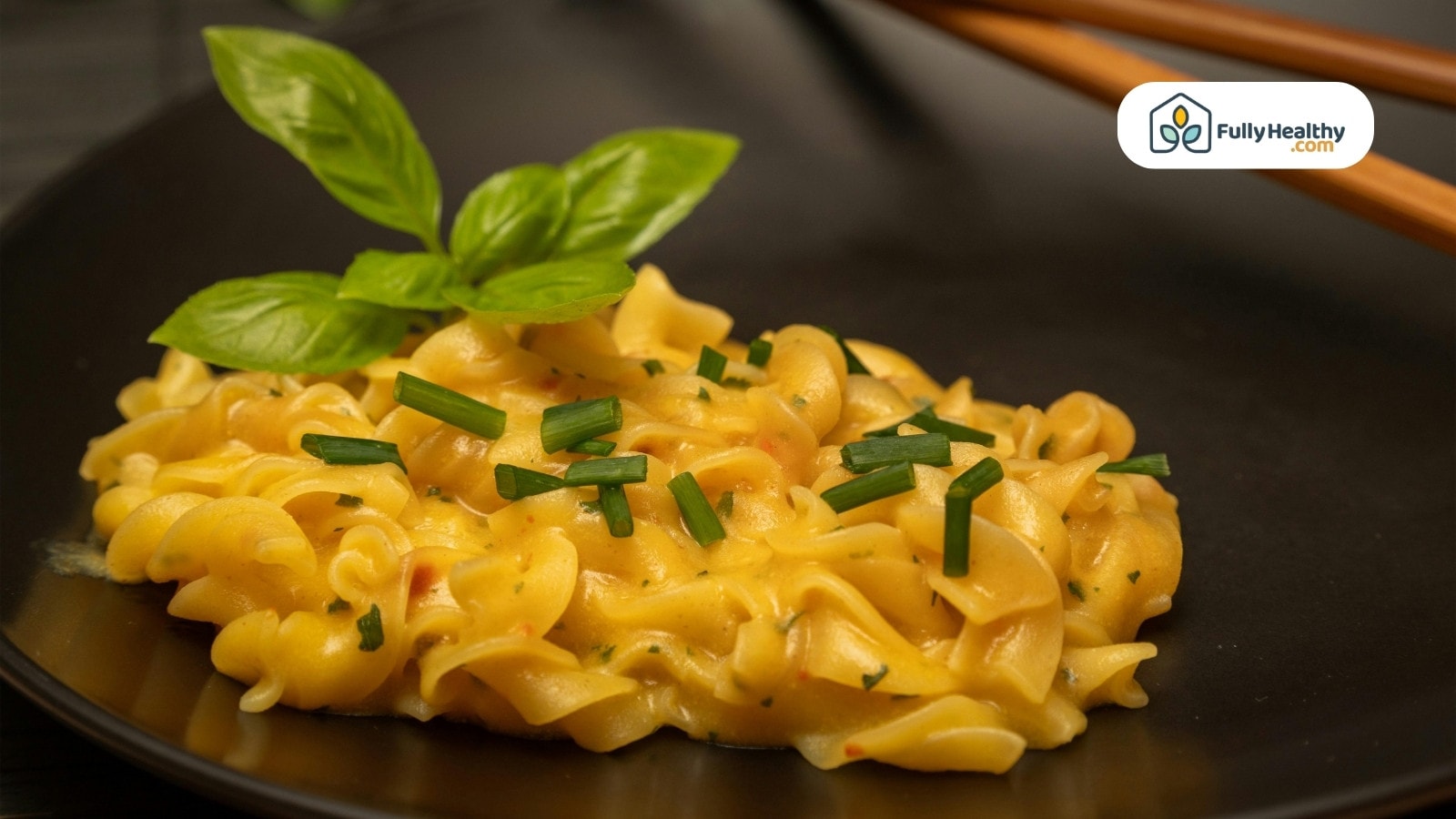 Creamy pasta garnished with basil leaves on a black plate