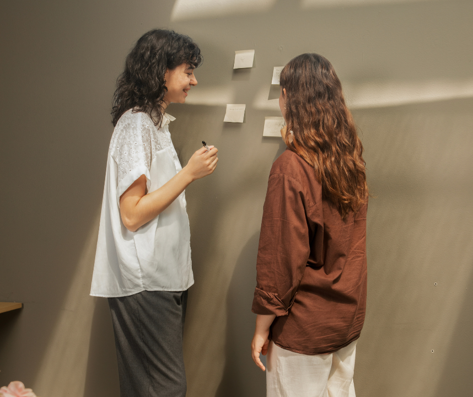 two women write on post-it notes on a wall as they examine a sales opportunity