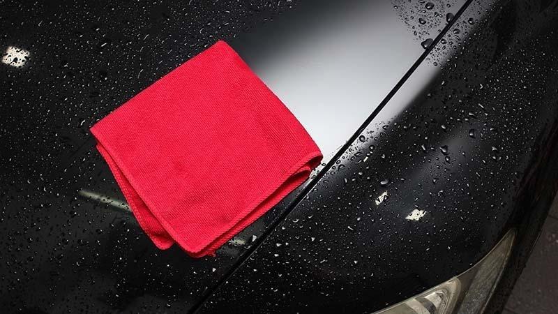 Drying a wet black car with a red microfiber towel