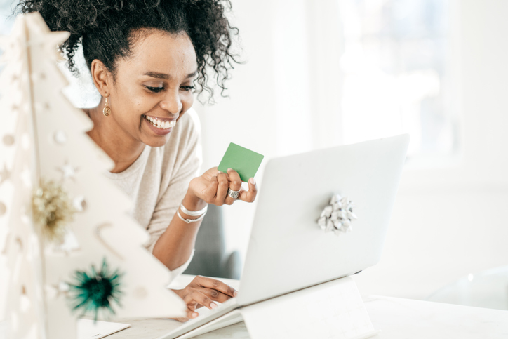 Beautiful African American woman shopping online with a Christmas tree next to her. 