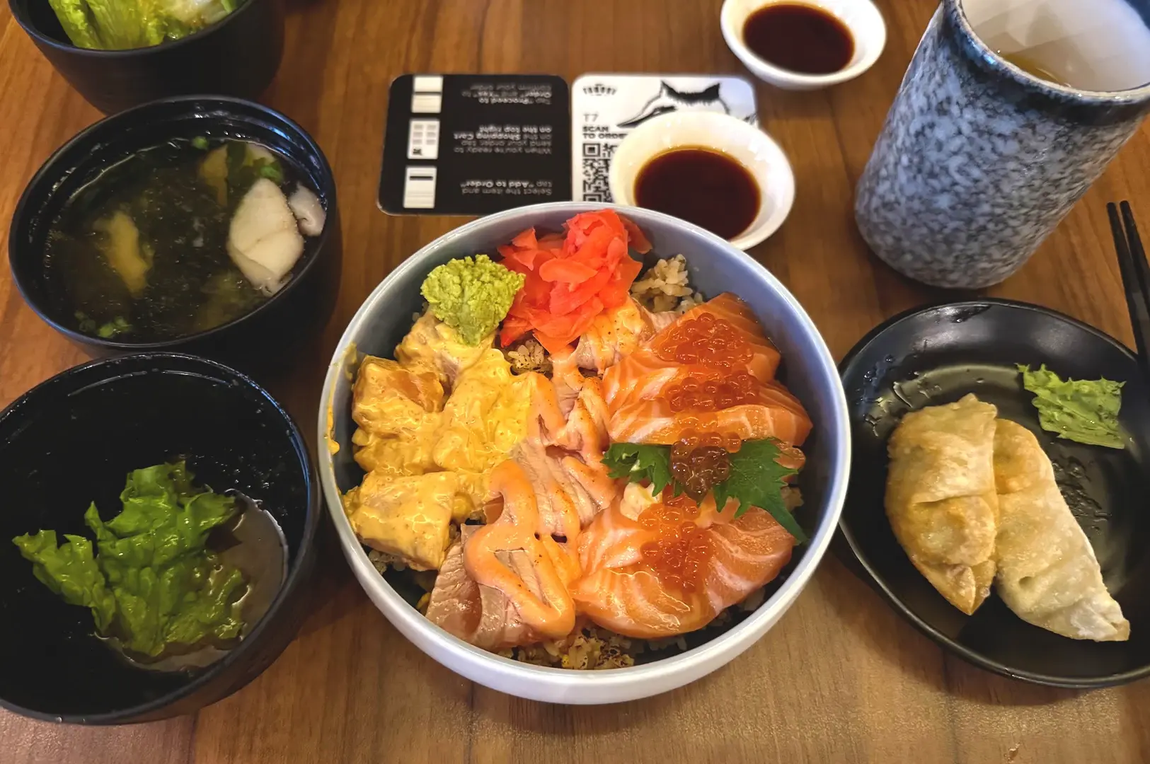 Tanuki Raw at Orchard Central, showcasing their popular Triple Salmon donburi served with miso soup and side dishes.