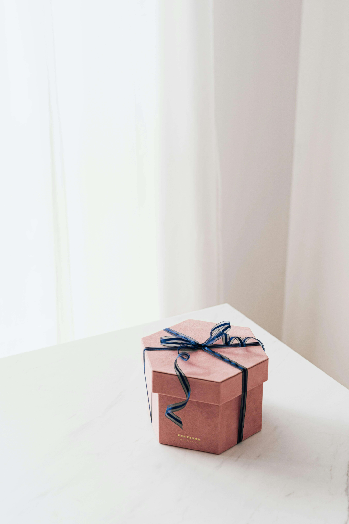 Pink hexagon gift box with a blue ribbon on a white marble surface.