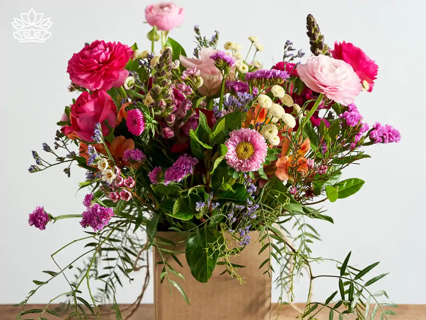 Exquisite bouquet of Secretary's Day flowers including vibrant pink roses, deep red carnations, delicate lavender, and an array of green foliage, all beautifully arranged in a rustic brown paper bag. 