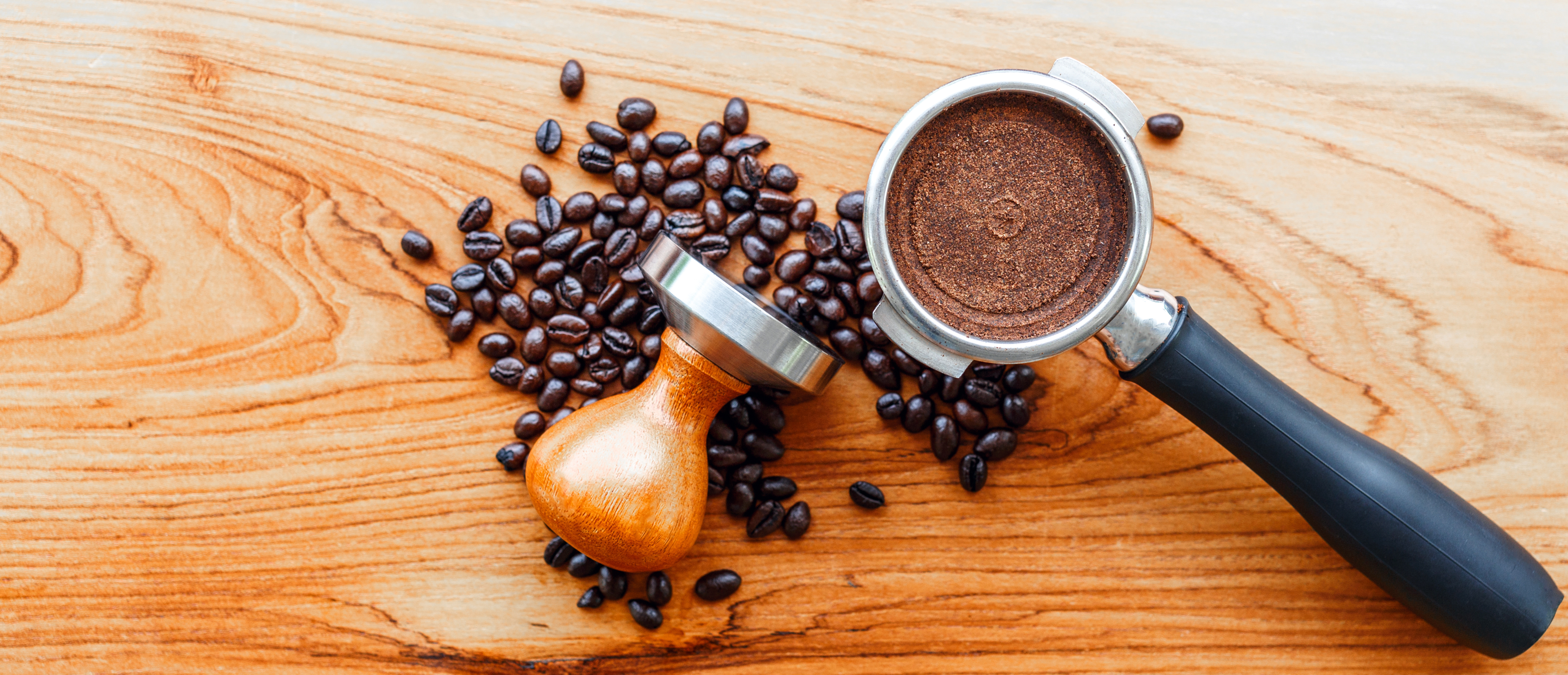 coffee portafilter tool, tamper, and roasted coffee beans on wooden background